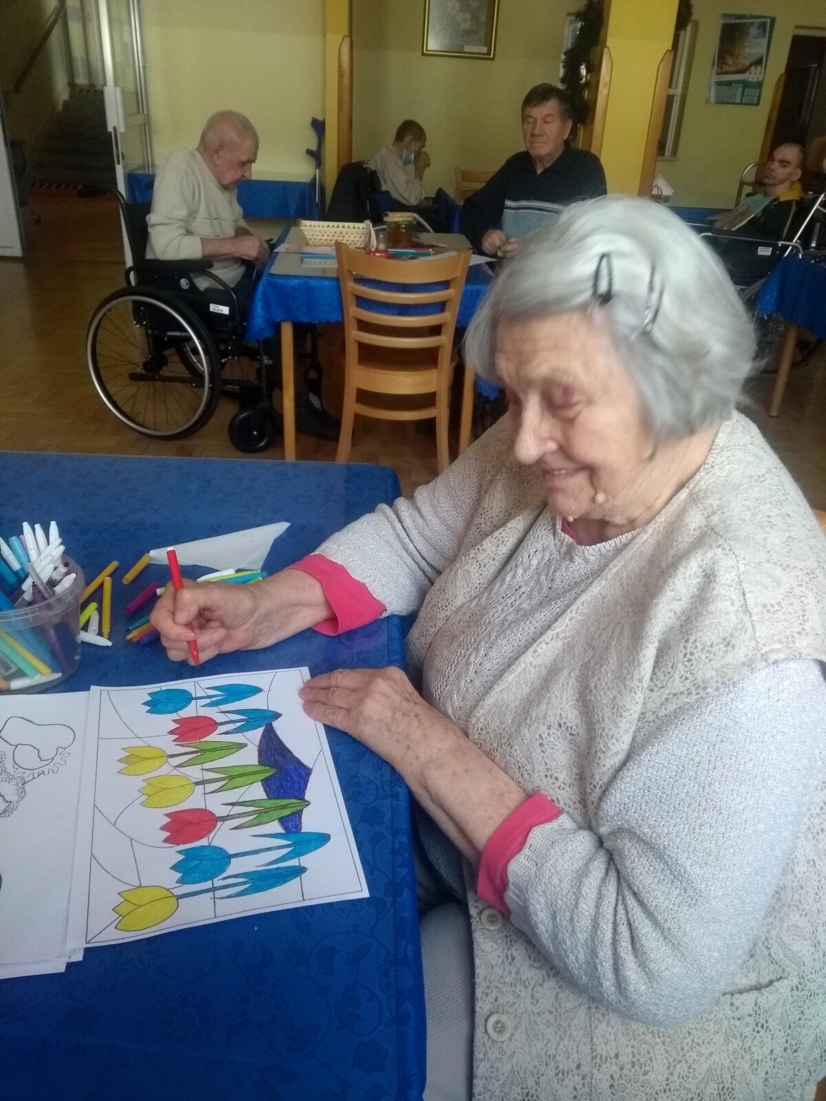 Uśmiechnięta starsza kobieta koloruje obrazek.