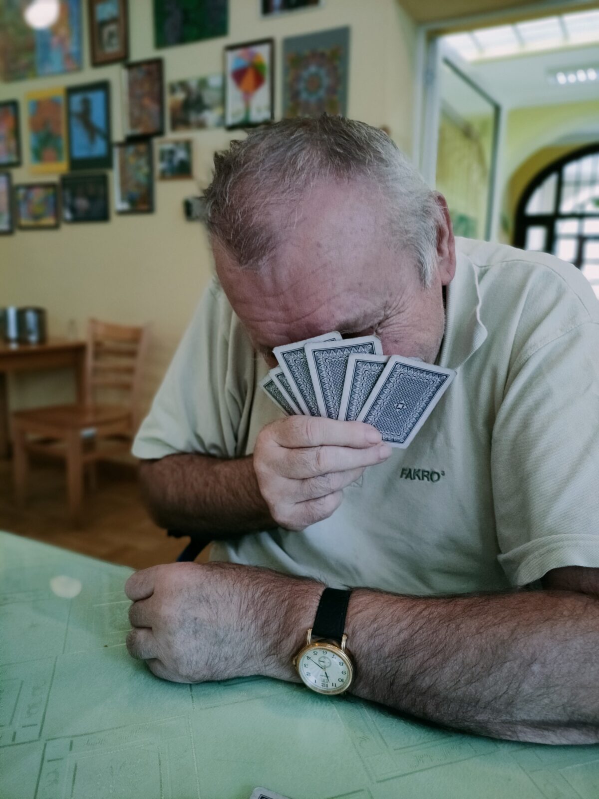 Mężczyzna siedzi przy stole, zakrywa twarz kartami.