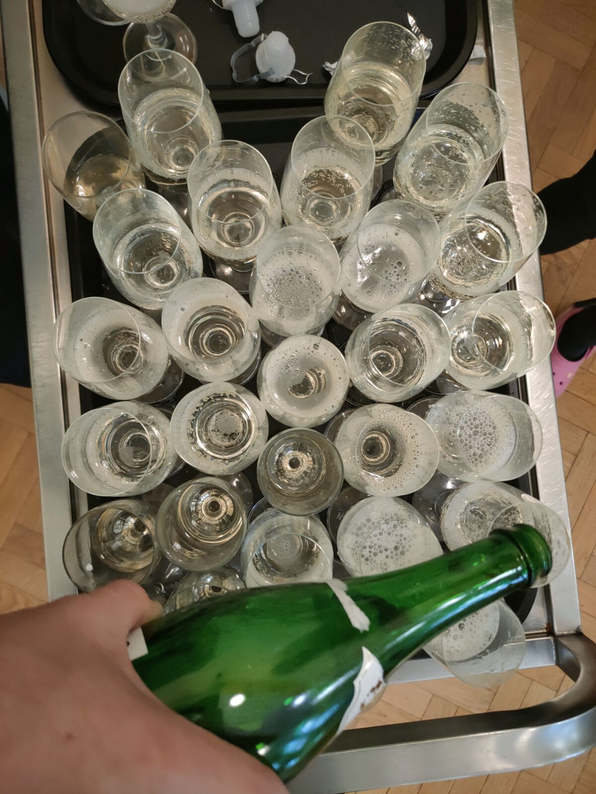 Na zdjęciu kieliszki z szampanem, zdjęcie wykonane od góry, u dołu zdjęcia widać butelkę i kawałek dłoni. 